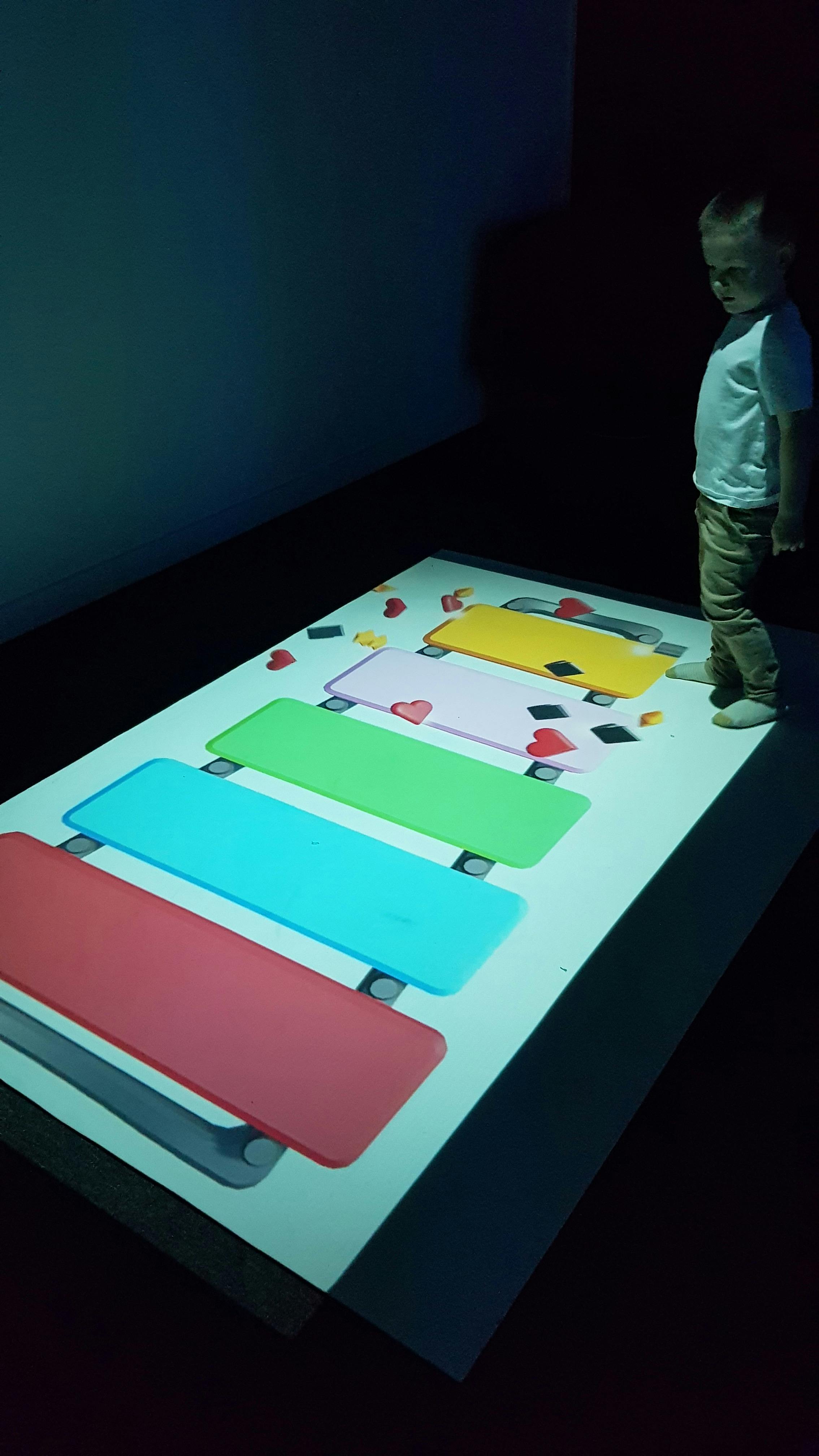 Young child moving his body to interact with a large-format digital game projected onto a floor.