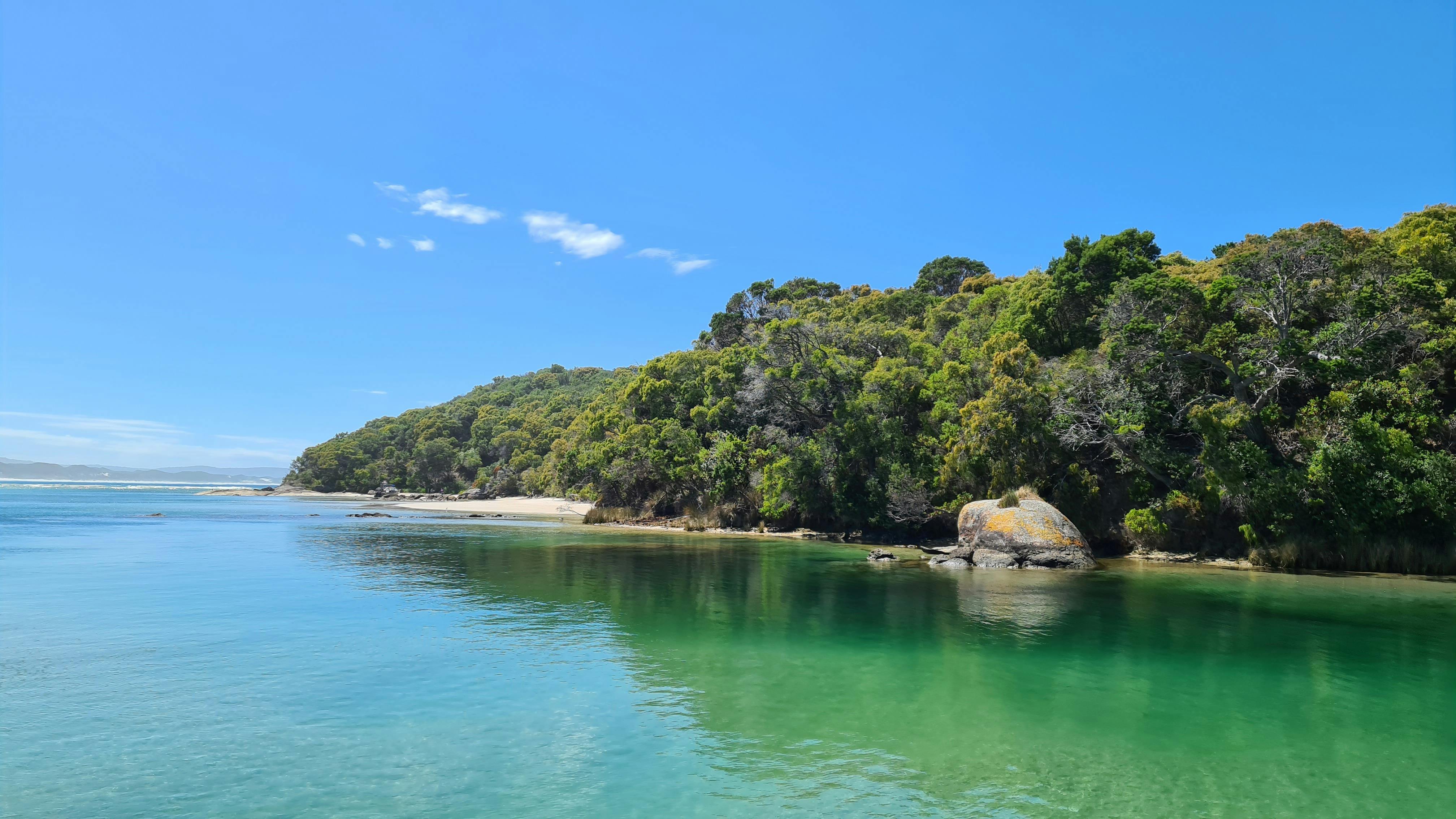 View from boat of calm water surrounding white sand island covered in trees