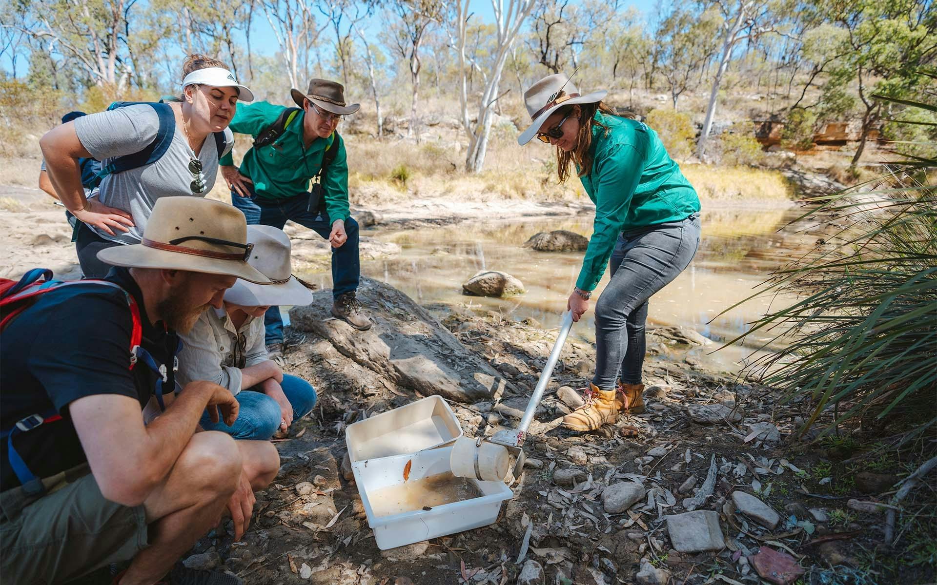 A group of people watching as an ecologist collects a sample of water from the river