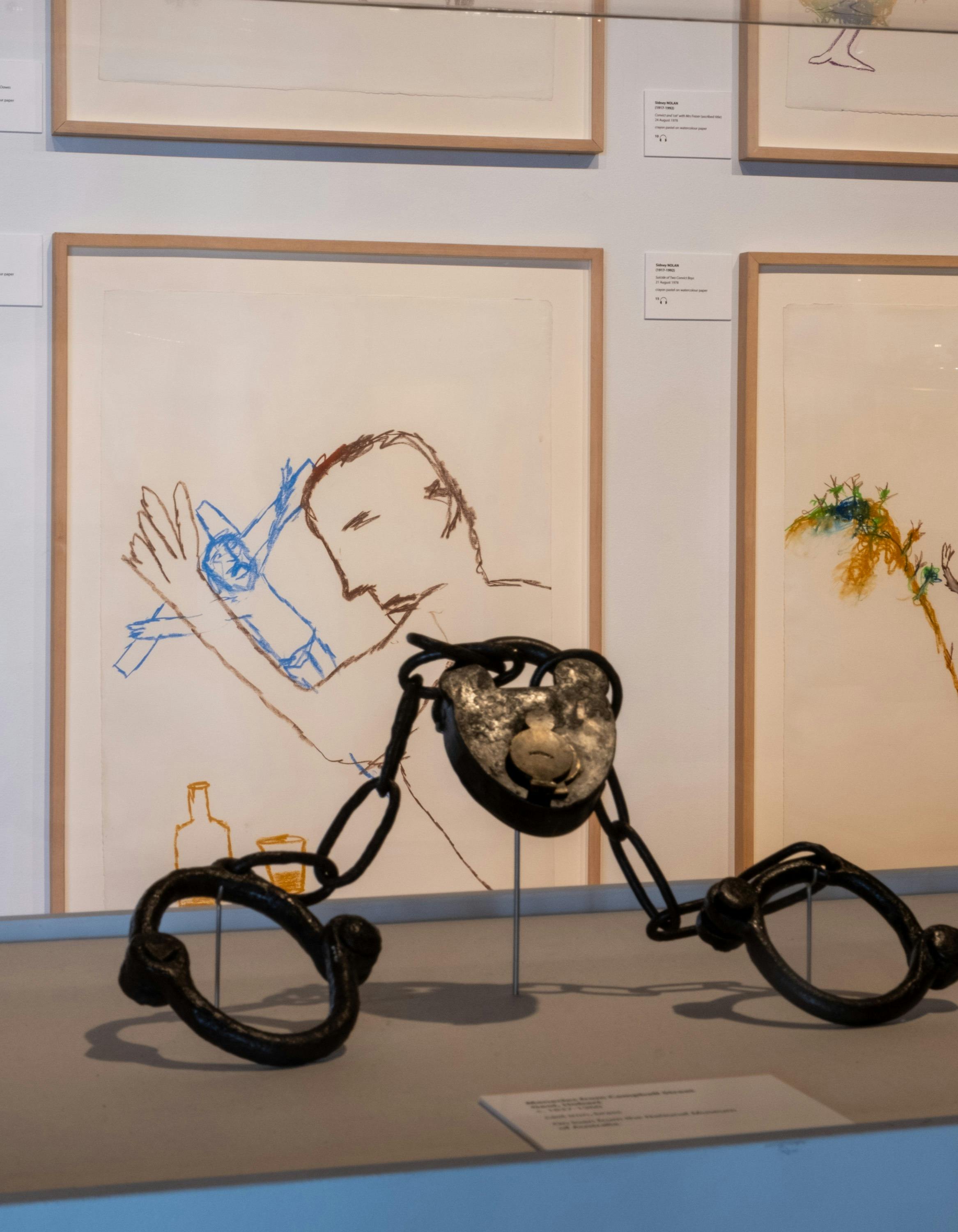 Installation image of convict cuffs with artworks by Sidney Nolan in background