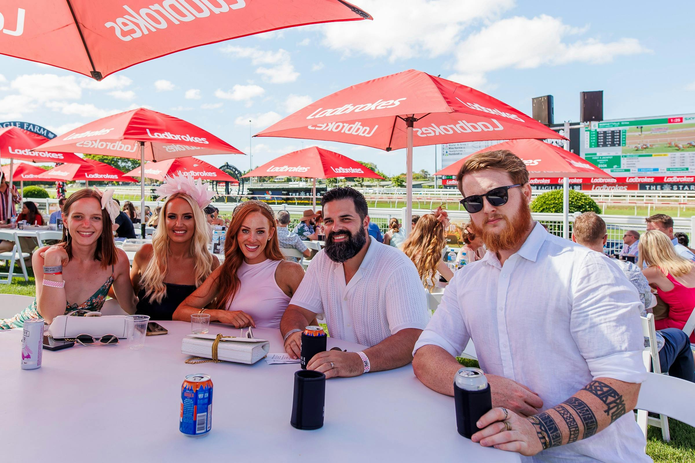 A group of people at a table on the lawn under Ladbrokes umbrellas
