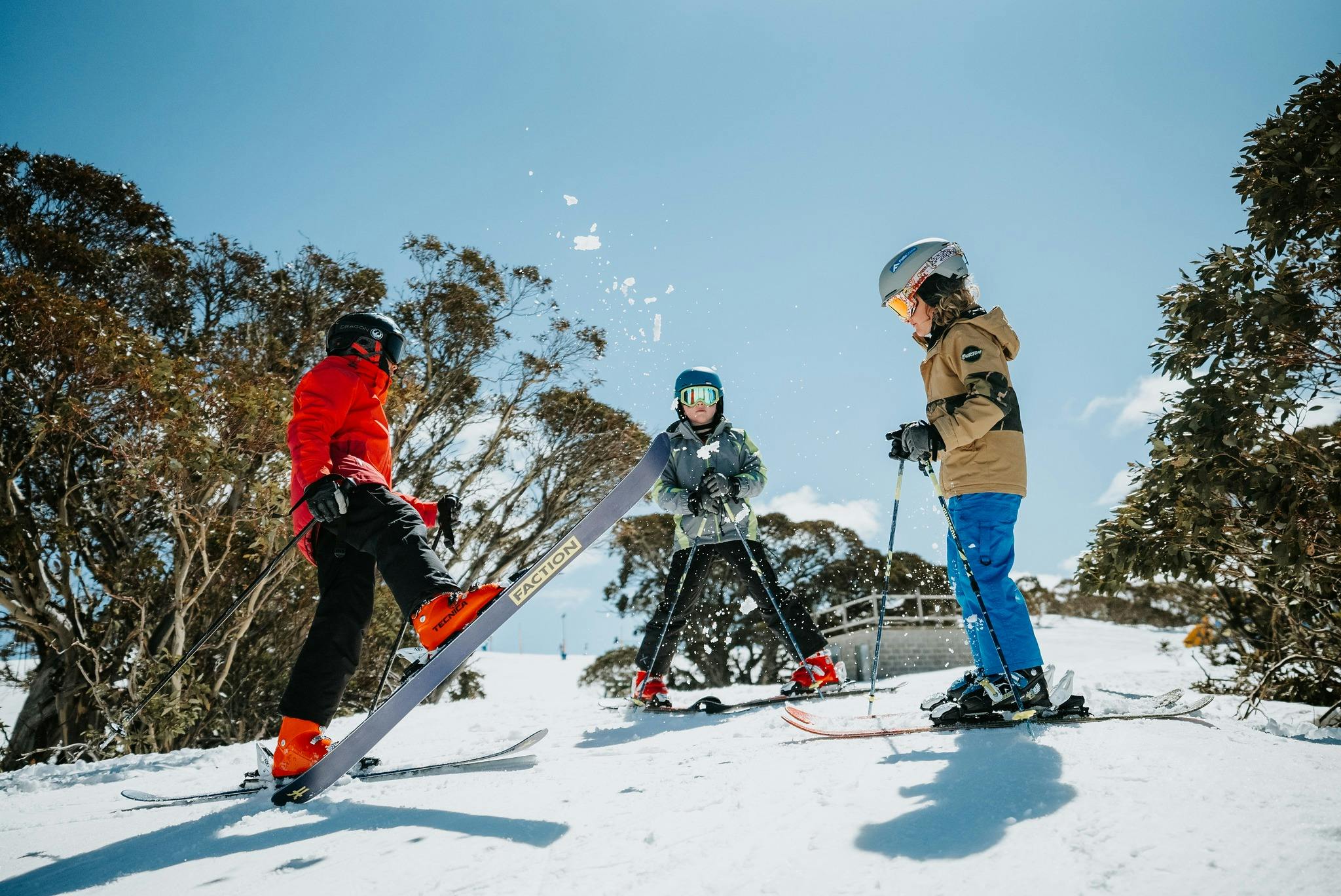 Three skier kids stand together before dropping into a ski run at falls creek on a sunny day.