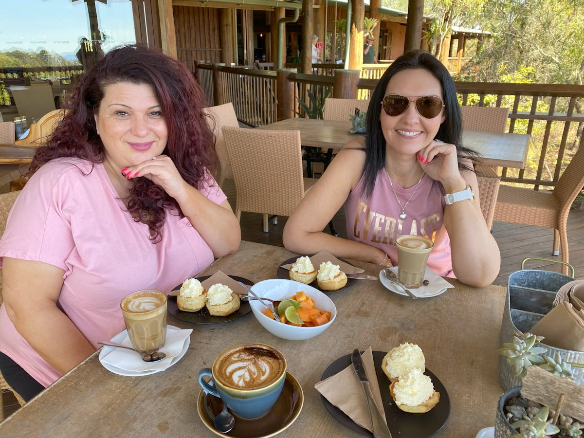 Two ladies sitting on the back deck enjoy scones with papaya jam and cream, skybury coffee and fruit