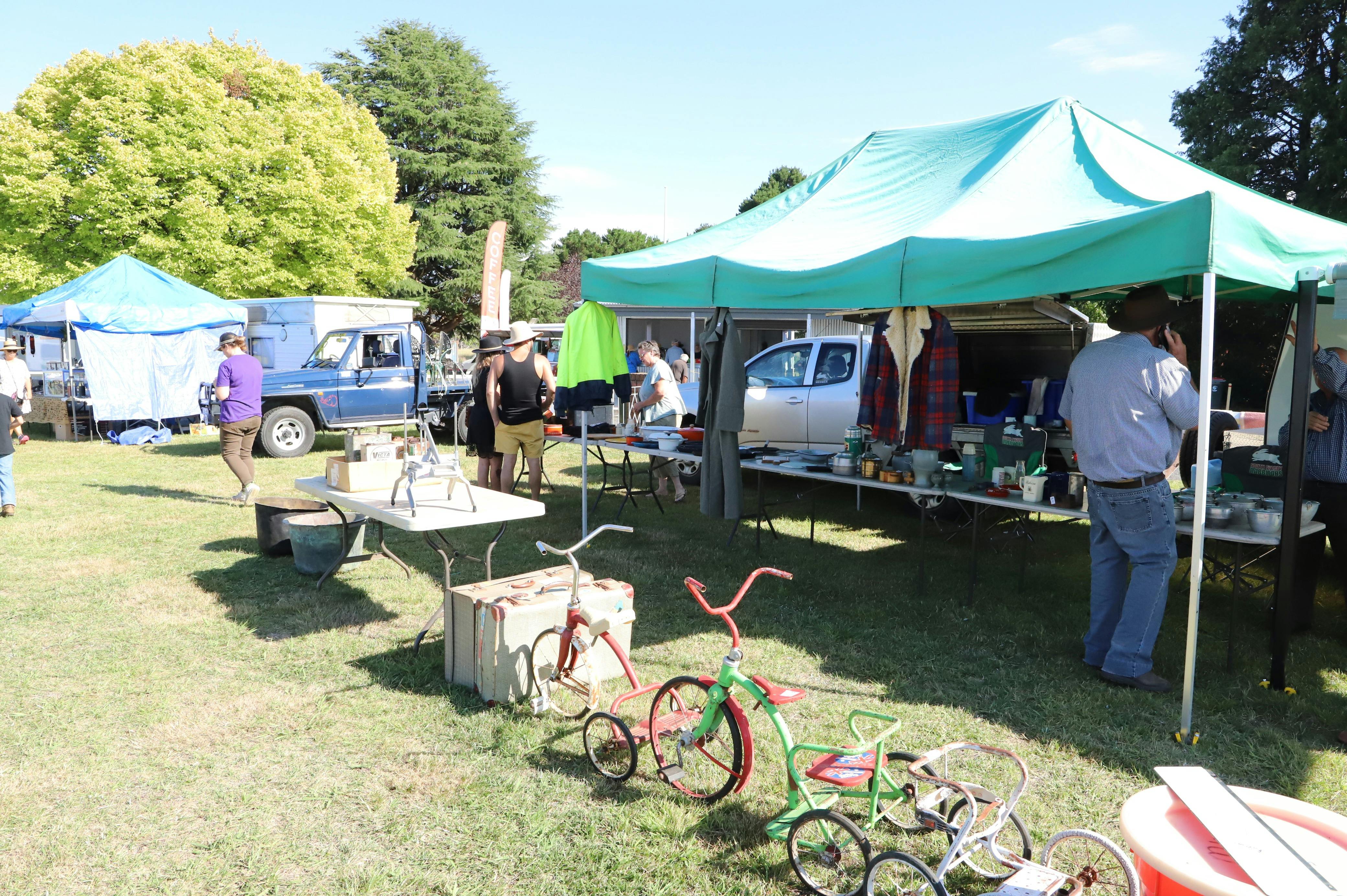 A green marquee in background and childrens tricycles in foreground on grassy area