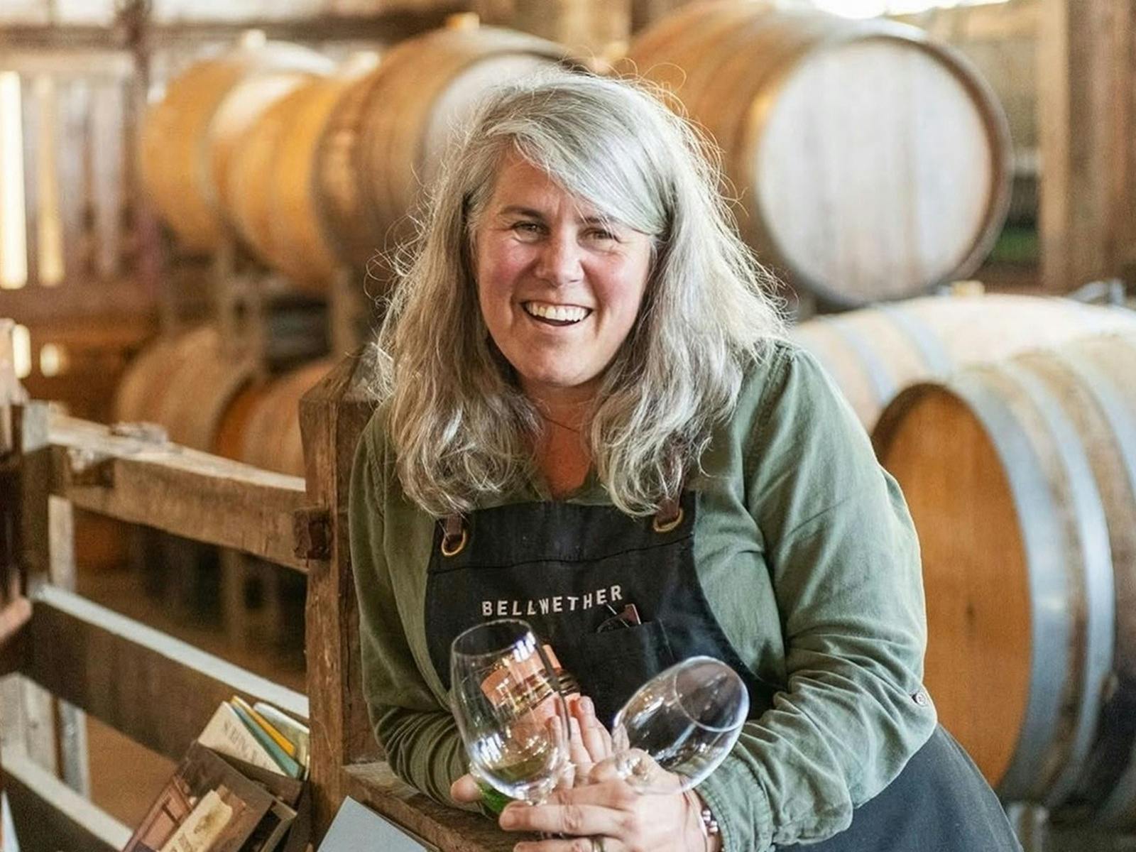A woman standing in front of wine barrels holding a wine glass smiling