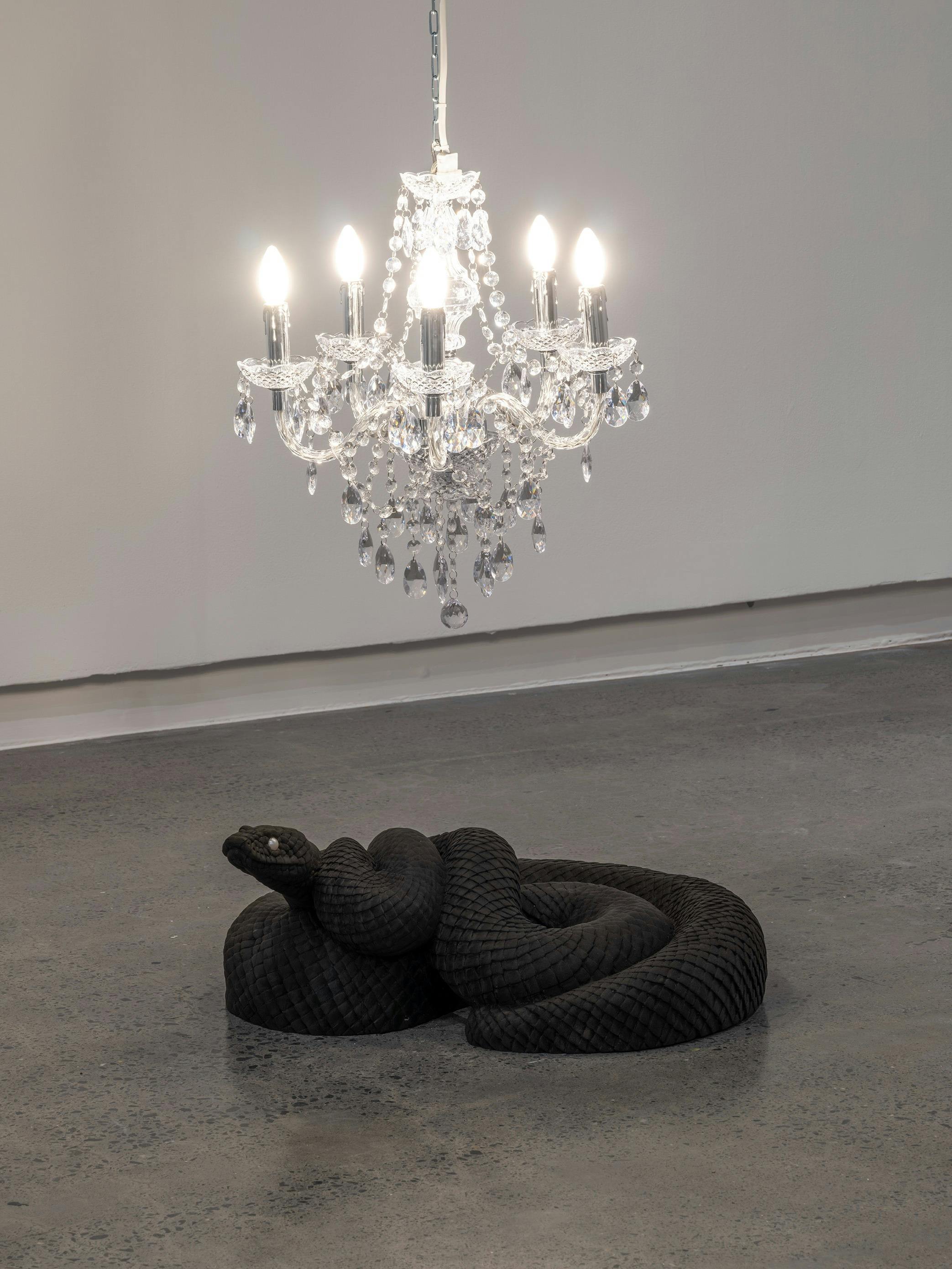 A sculptural black python with pearl eyes under a lit chandelier.