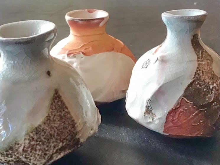 3 bottles on charcoal table, white with orange and brown accents, light shining from left