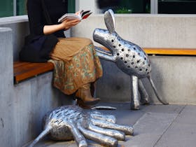 Two metal public sculptures of dogs with woman reading