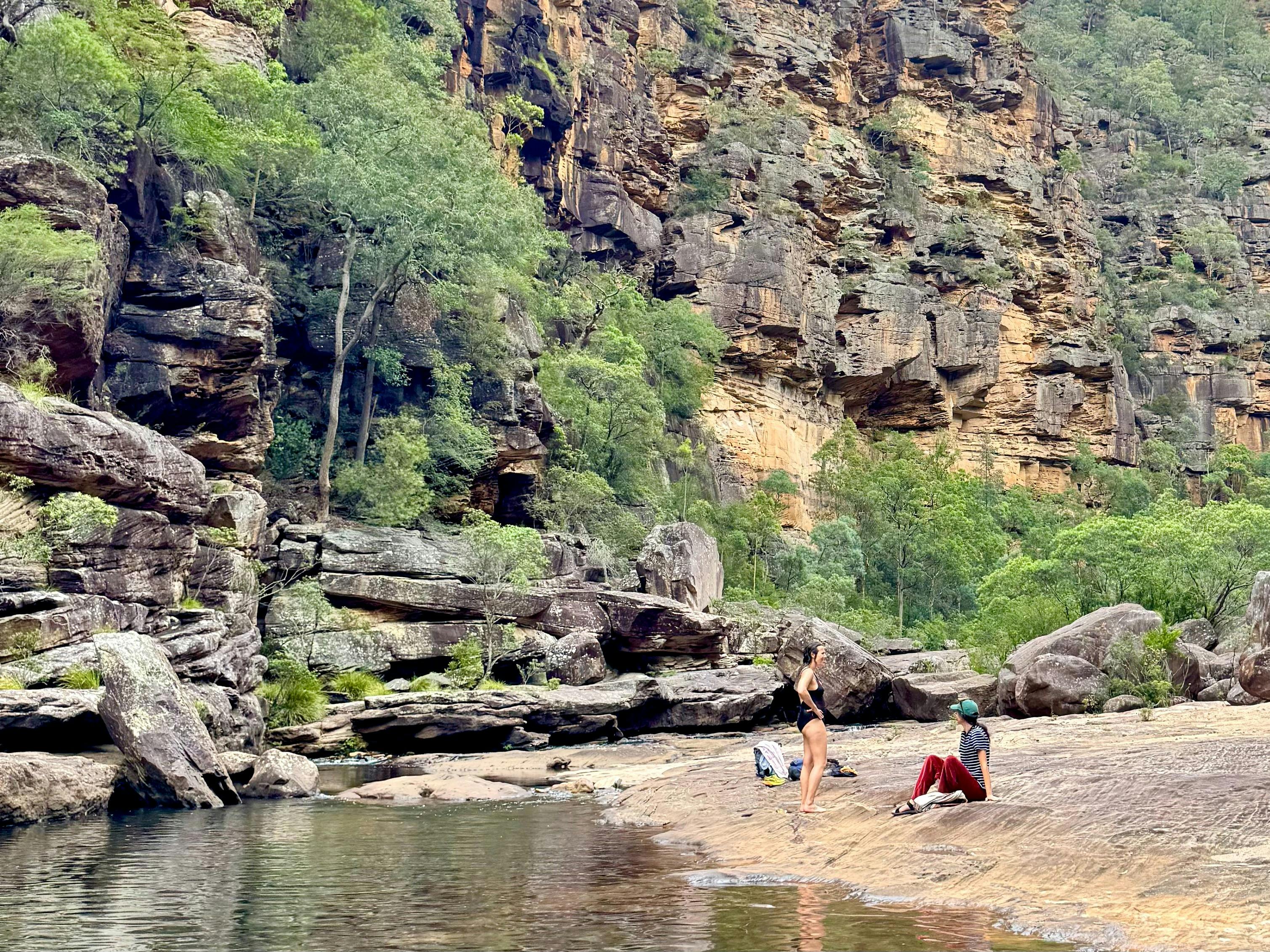 2 women chat by the water among cliffs and Australian fauna