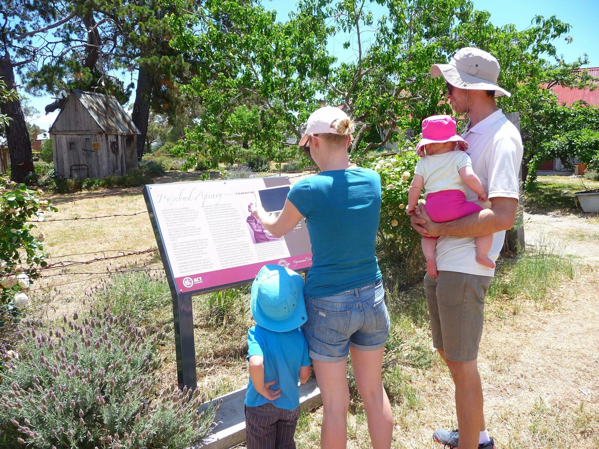 Woman holding device infront of sign with man and two children