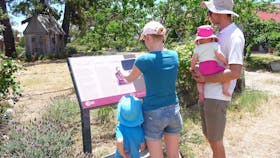 Woman holding device infront of sign with man and two children