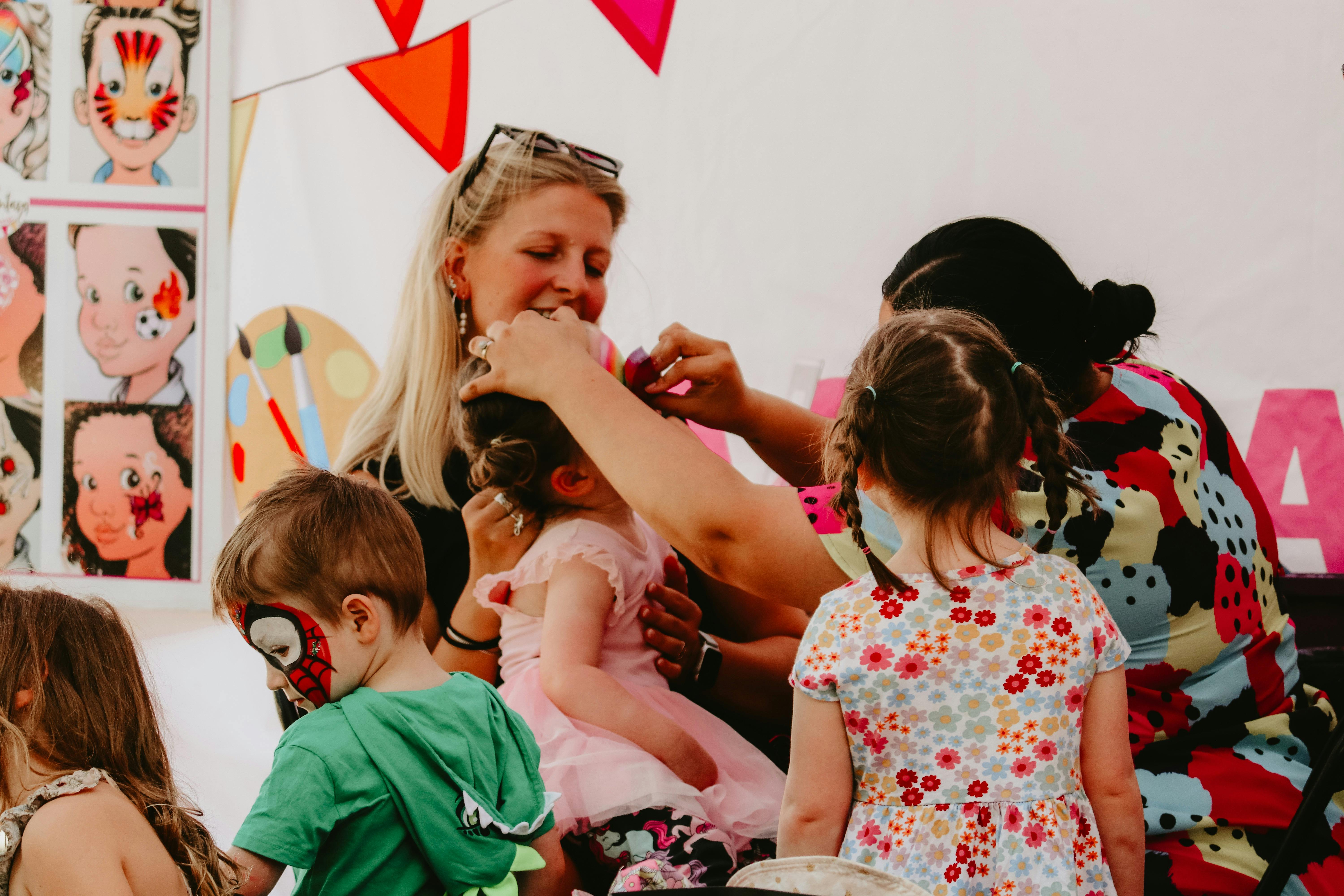 Children getting their facepainted whilst a smiling woman watches on