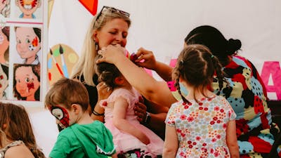 Children getting their facepainted whilst a smiling woman watches on