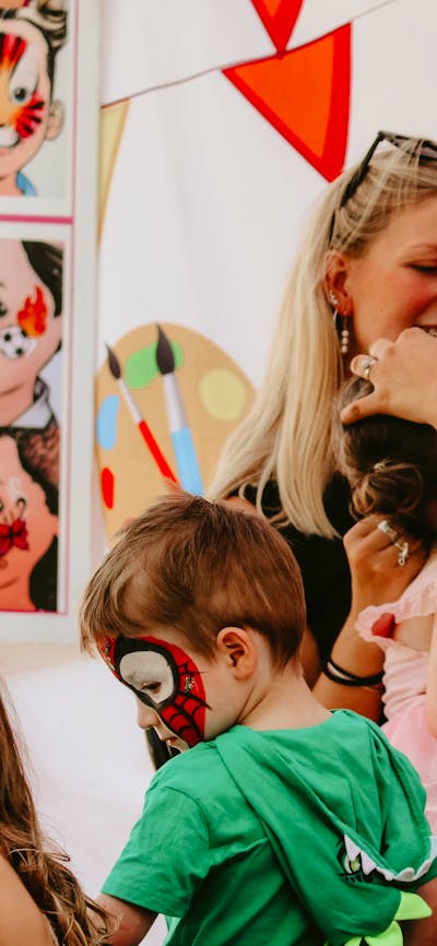 Children getting their facepainted whilst a smiling woman watches on
