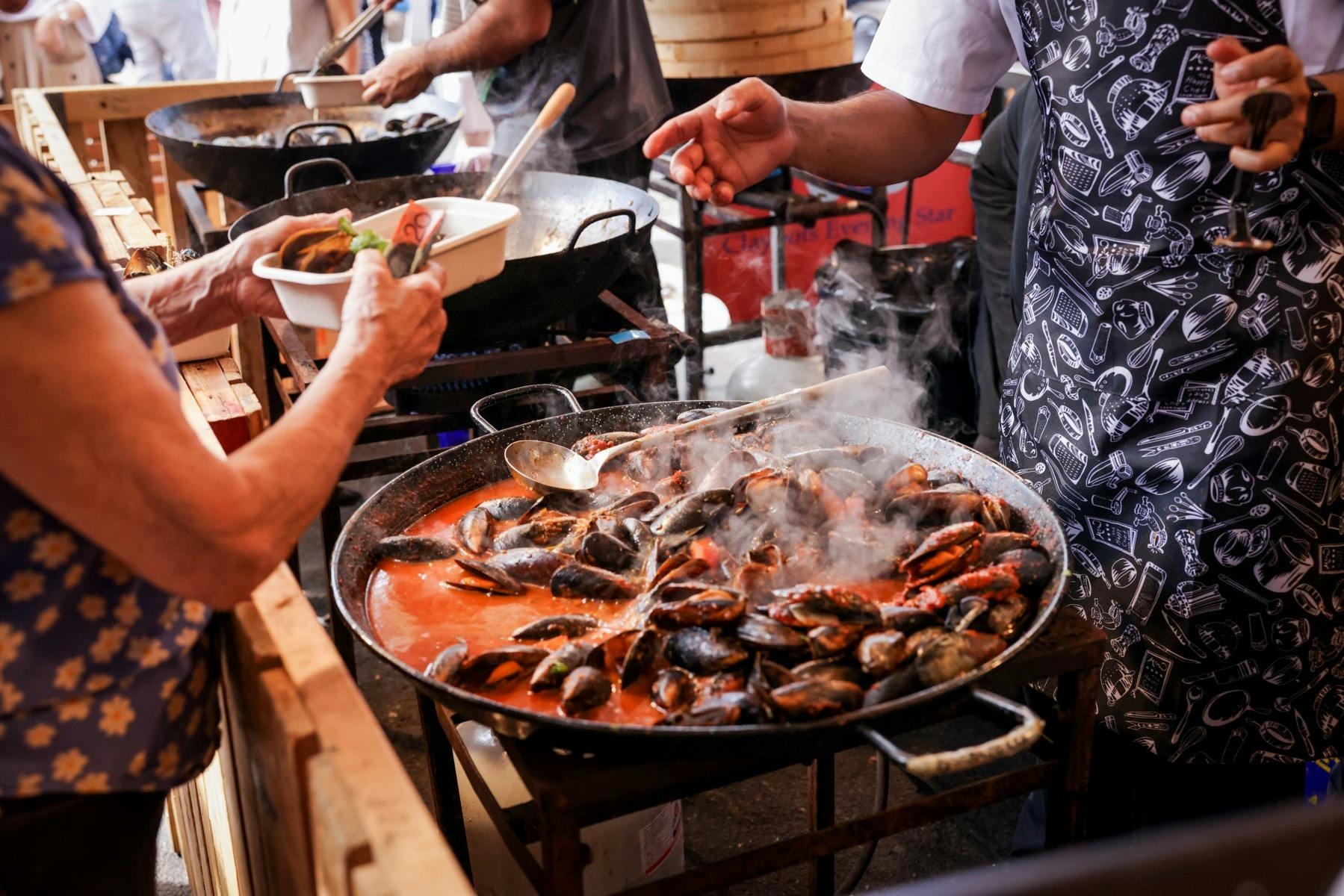 Mussels being cooked in a large wok in tomato sauce