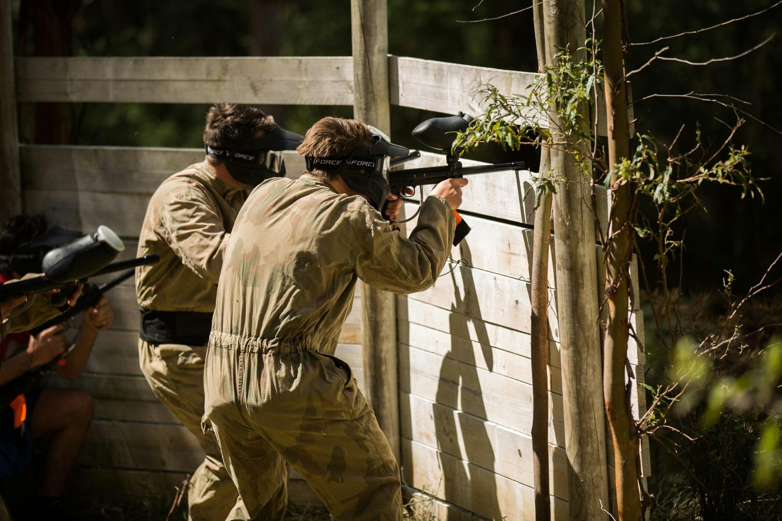 Phoenix Paintball - 2 players aim from behind a timber barricade