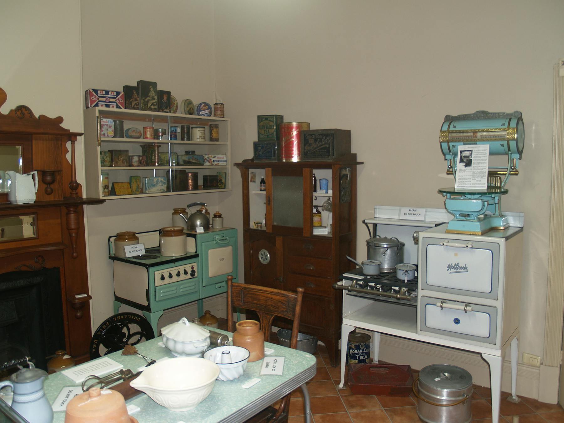 Kitchen display room showing 2 cast iron stoves, shop scales and a various collection of old tins