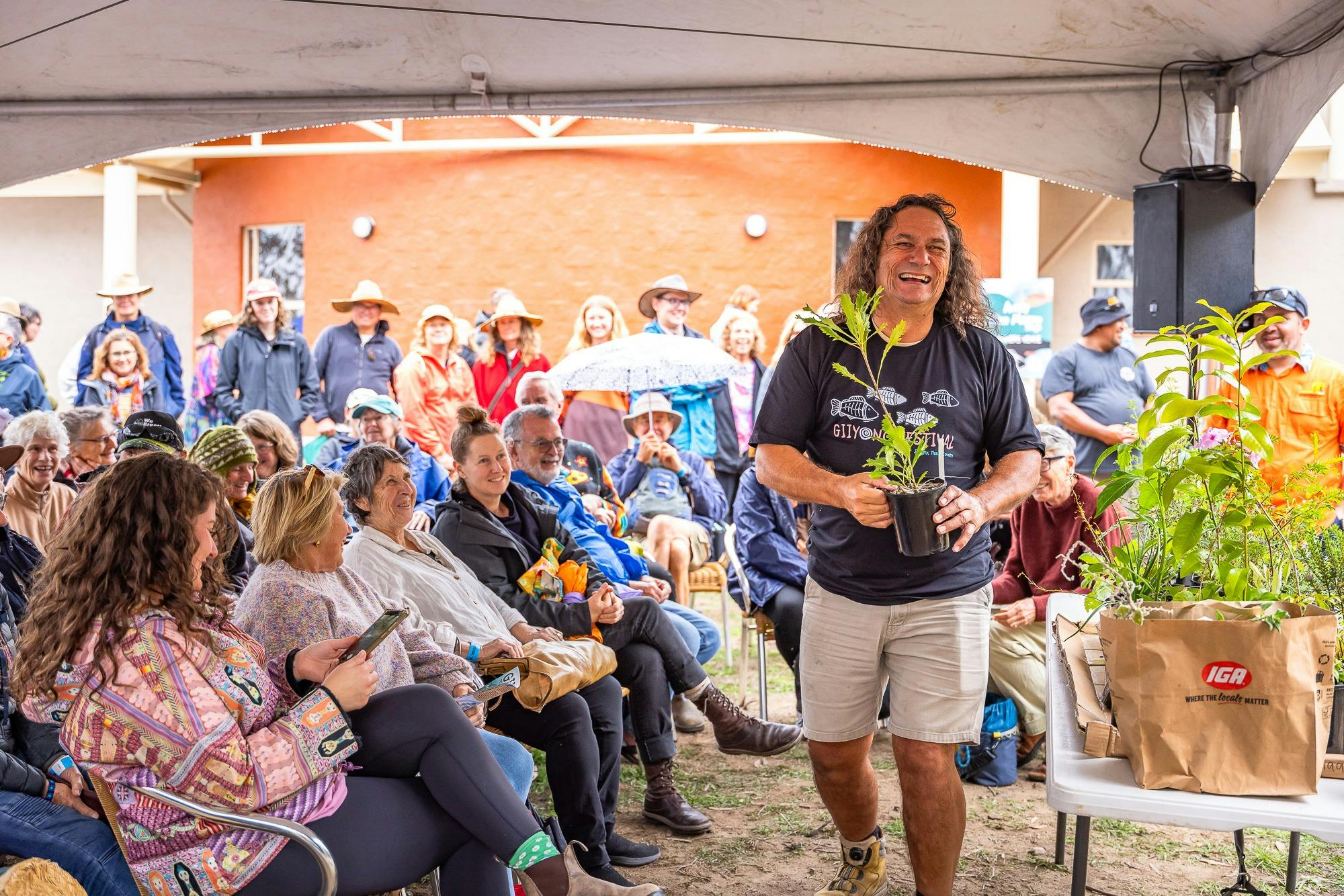 An Aboriginal man carries a native plant infront of an audience.