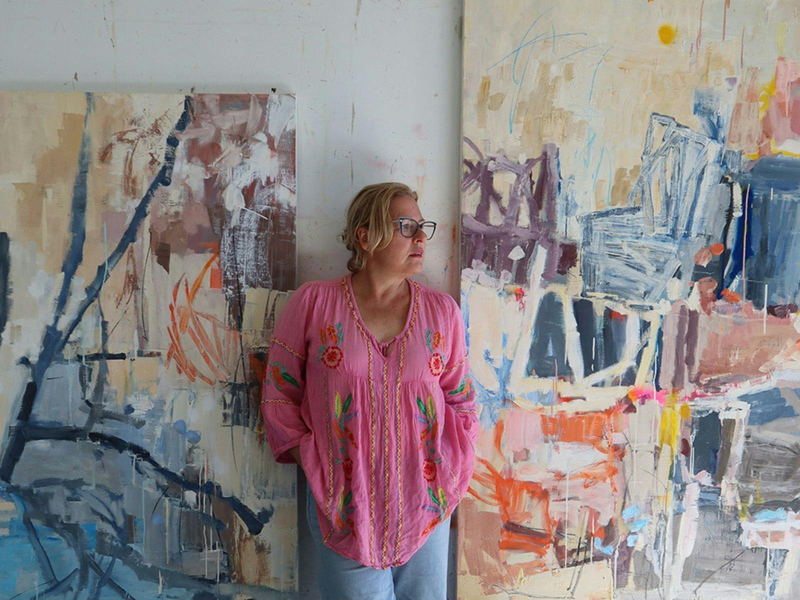 Artist Leah Thiessen standing in a studio next to her colourful abstract artworks.