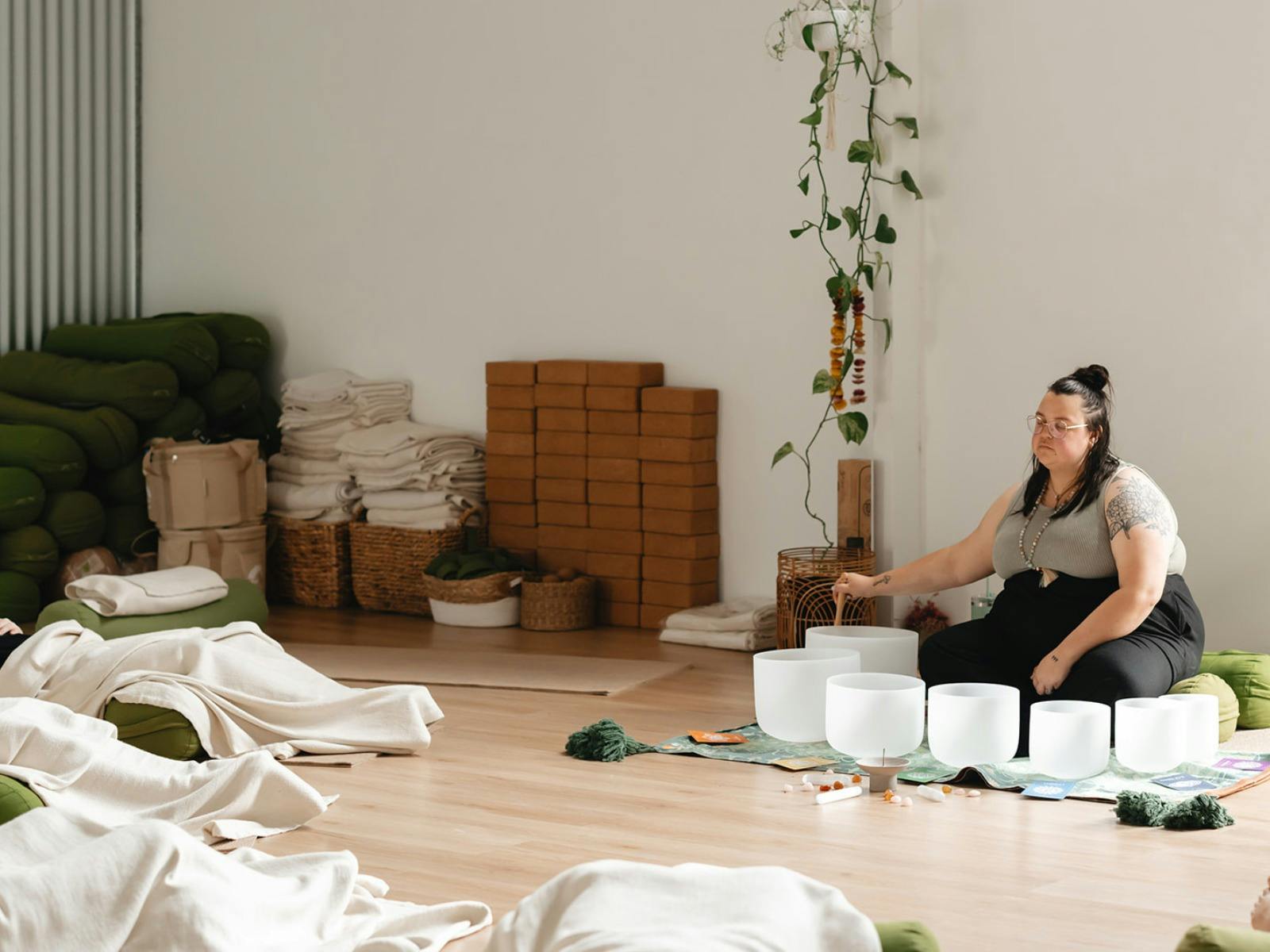 Sound healer playing crystal singing bowls in a serene studio with mats and blankets arranged.