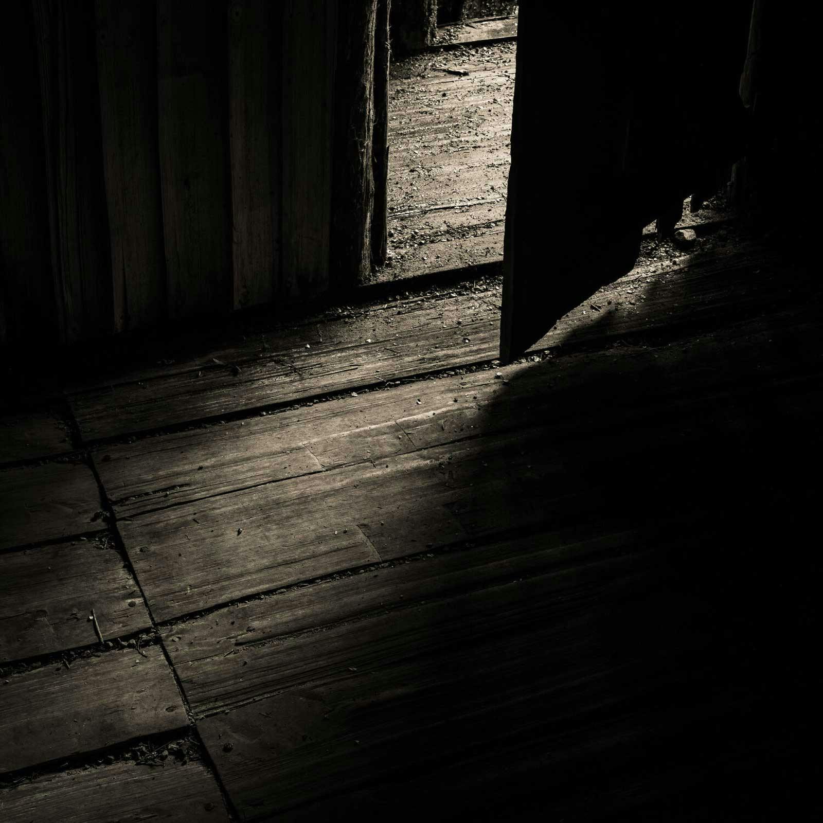 Sepia photograph of light coming through an open door highlighting the texture of the wood floor