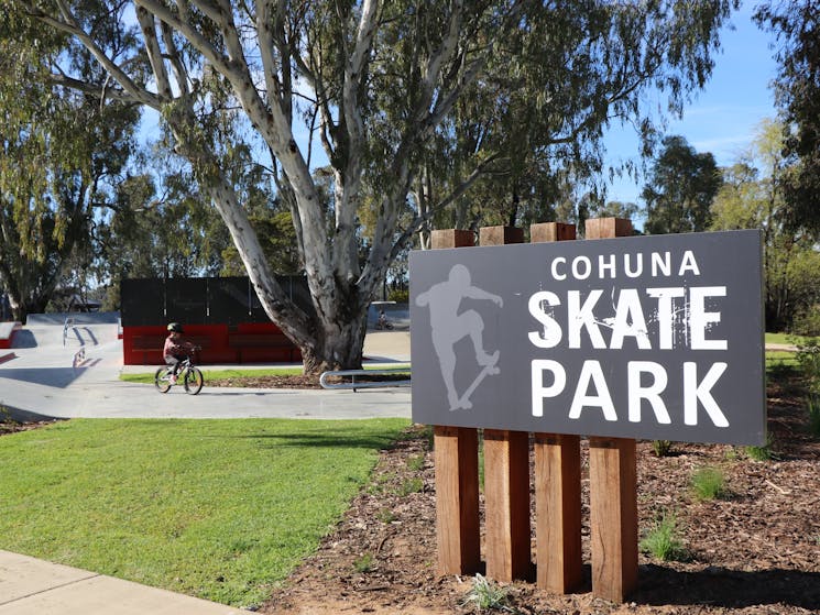 Cohuna Skate Park sign with young boy on bicycle in the background