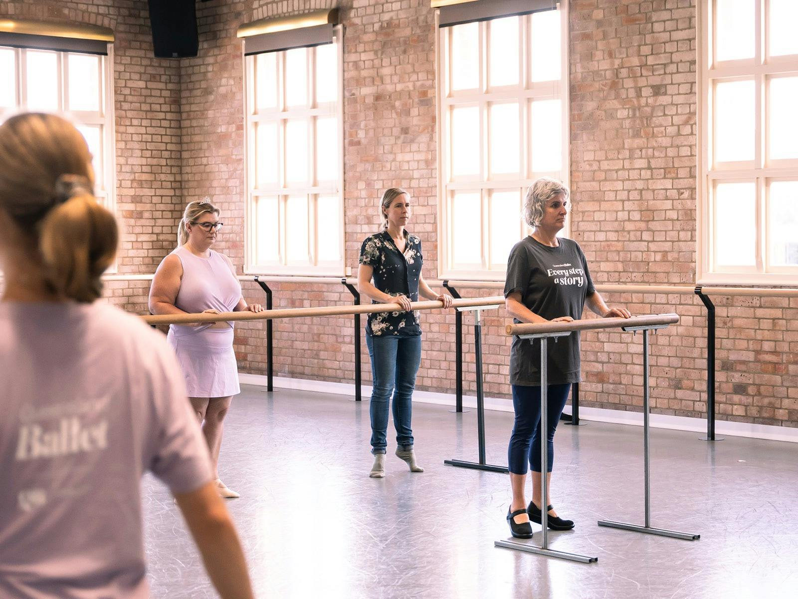3 ladies holding onto ballet barre on raised toes under the guidance of a Queensland Ballet teacher 3 ladies holding onto ballet barre on raised toes under the guidance of a Queensland Ballet teacher
