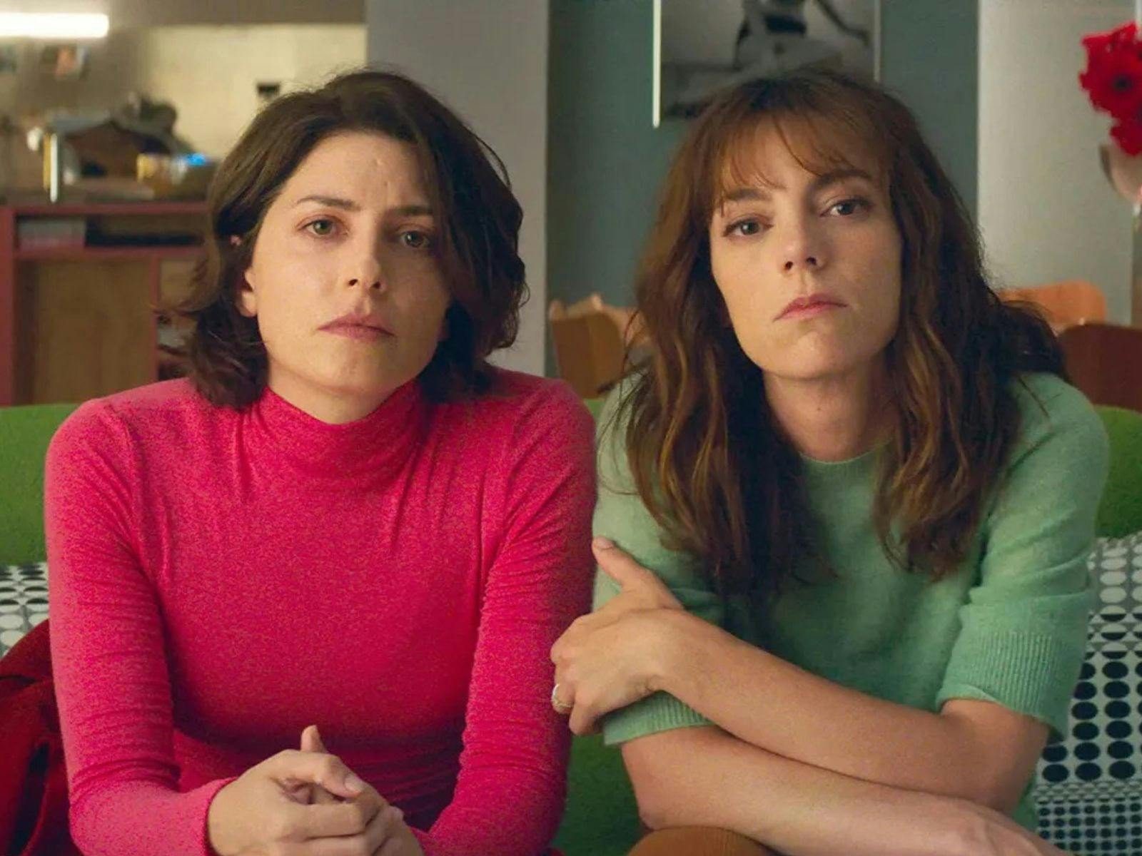 A woman with short brown hair and a pink top sits next to a woman with long brown hair and green top
