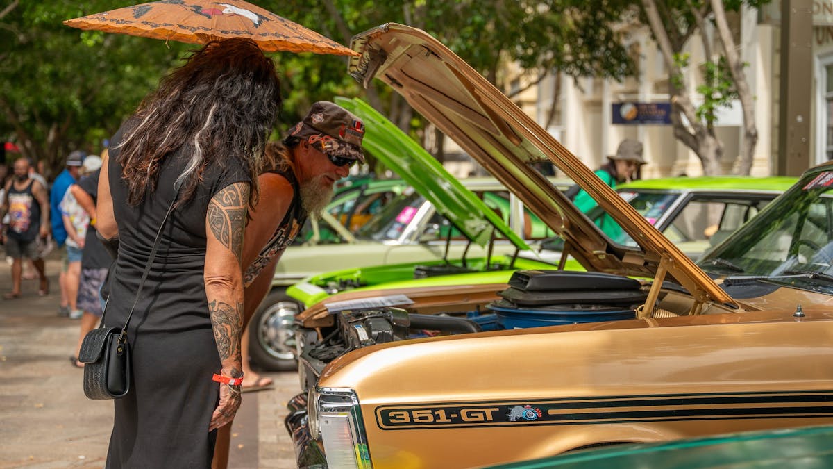 People viewing classic cars with open bonnets during Rockynats.