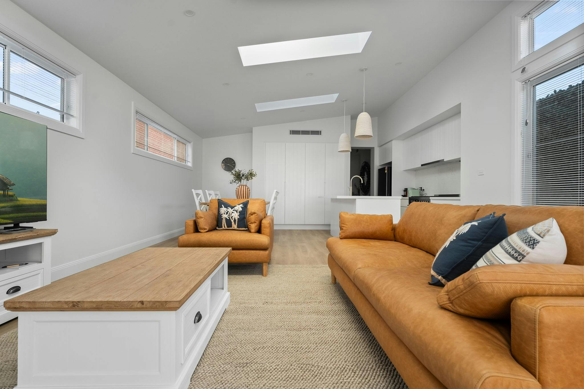 Brown leather couches and arm chair, with coffee table, rug, smart tv, dining area and kitchen