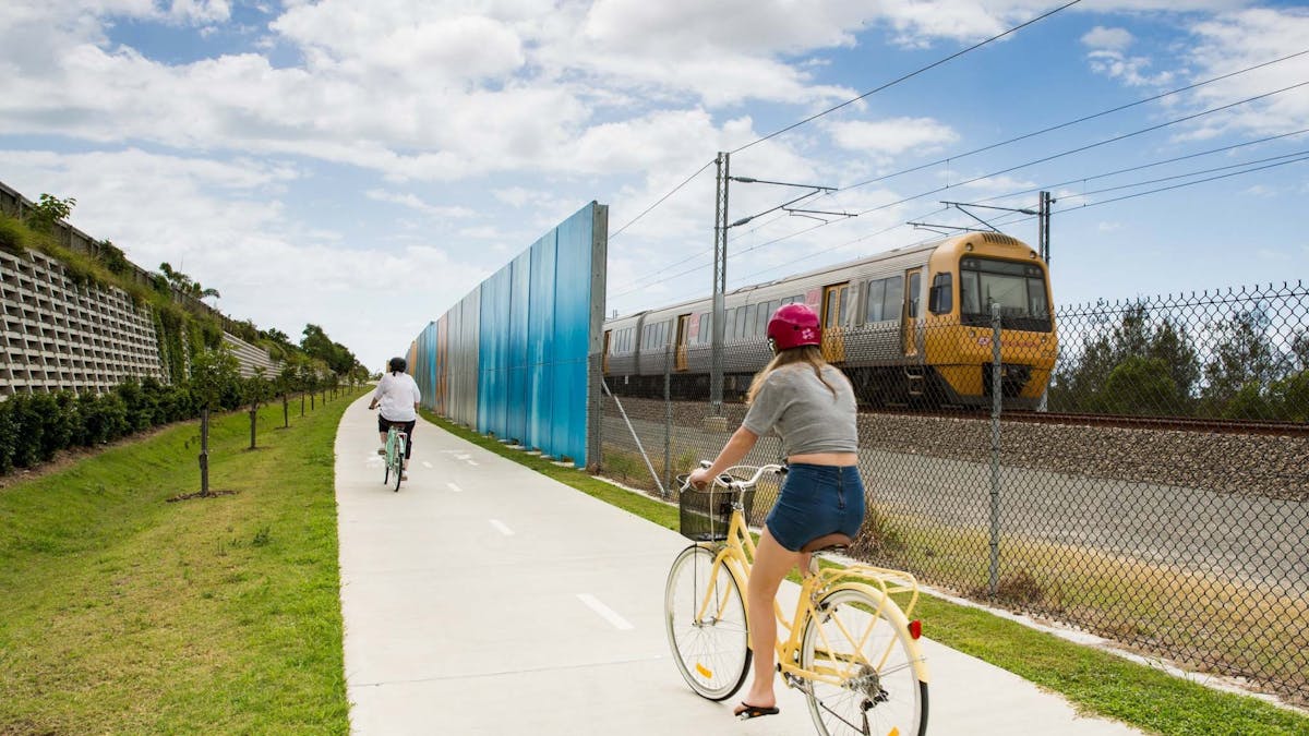 Two people taking a ride on the Petrie to Kippa-Ring Shared Pathway with a train on the tracks Two people taking a ride on the Petrie to Kippa-Ring Shared Pathway with a train on the tracks