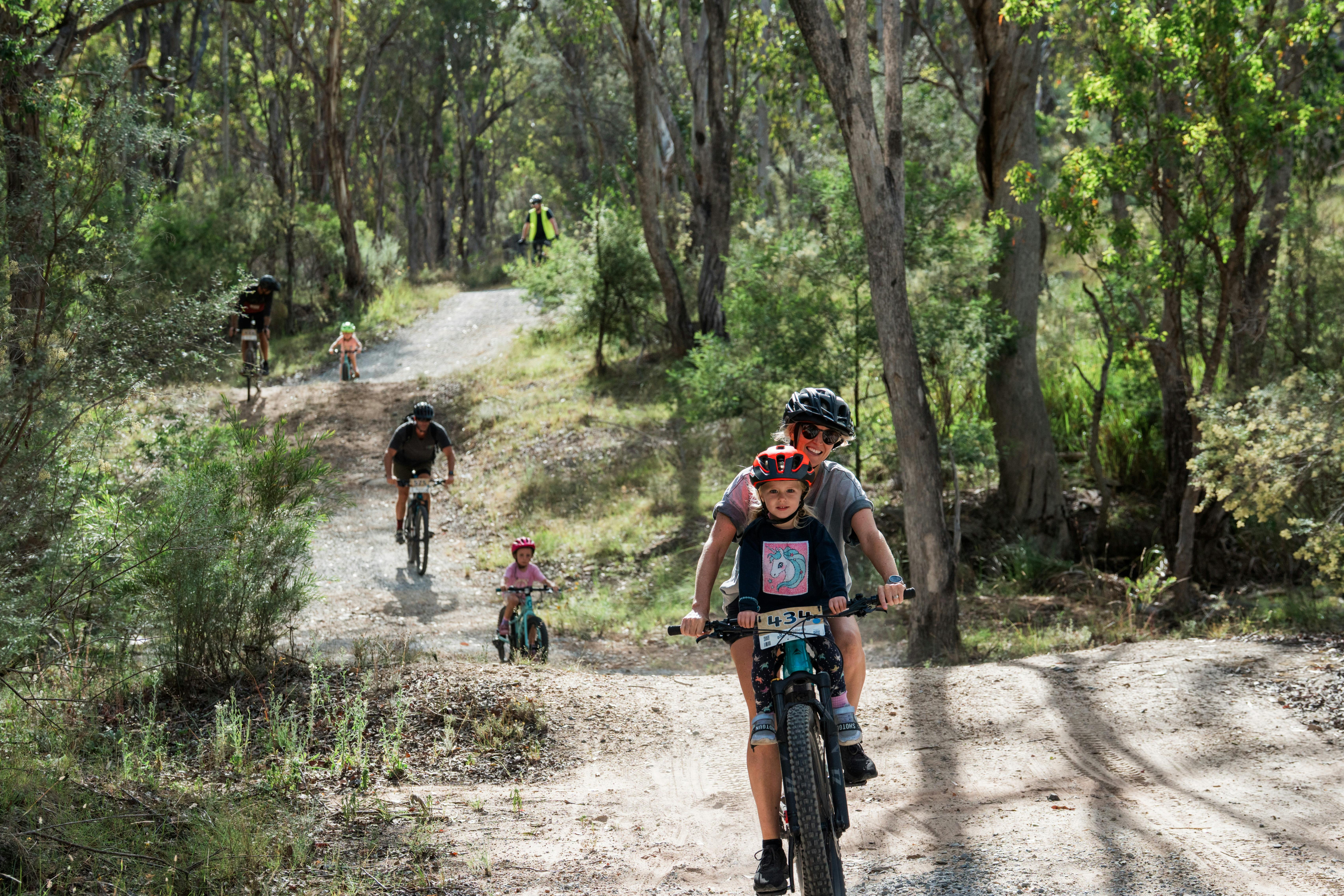 Child riding on bike seat with mum, with youth riders in the background on Curry