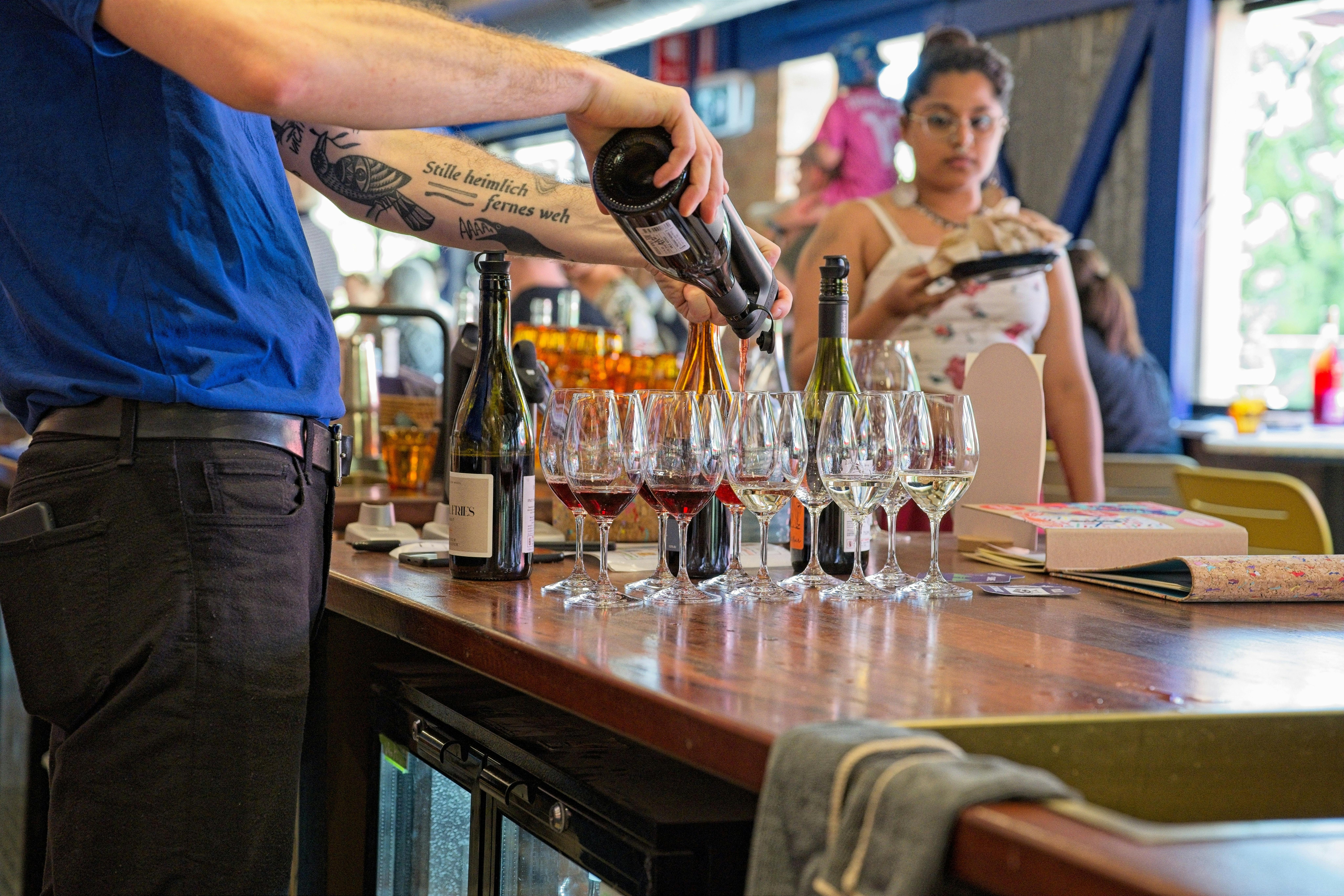 A staff member pours wine into several glasses for tasting