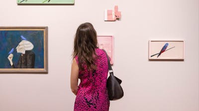 A person wearing a patterned dress views several painted portraits on a light-coloured wall.