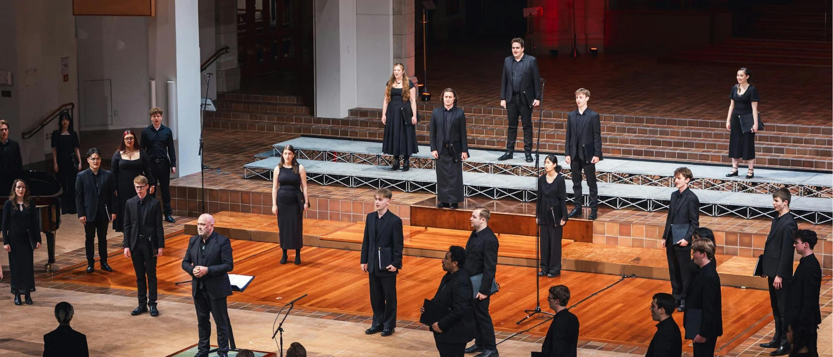 A group of singers dressed in black stand on a stage in front of microphones