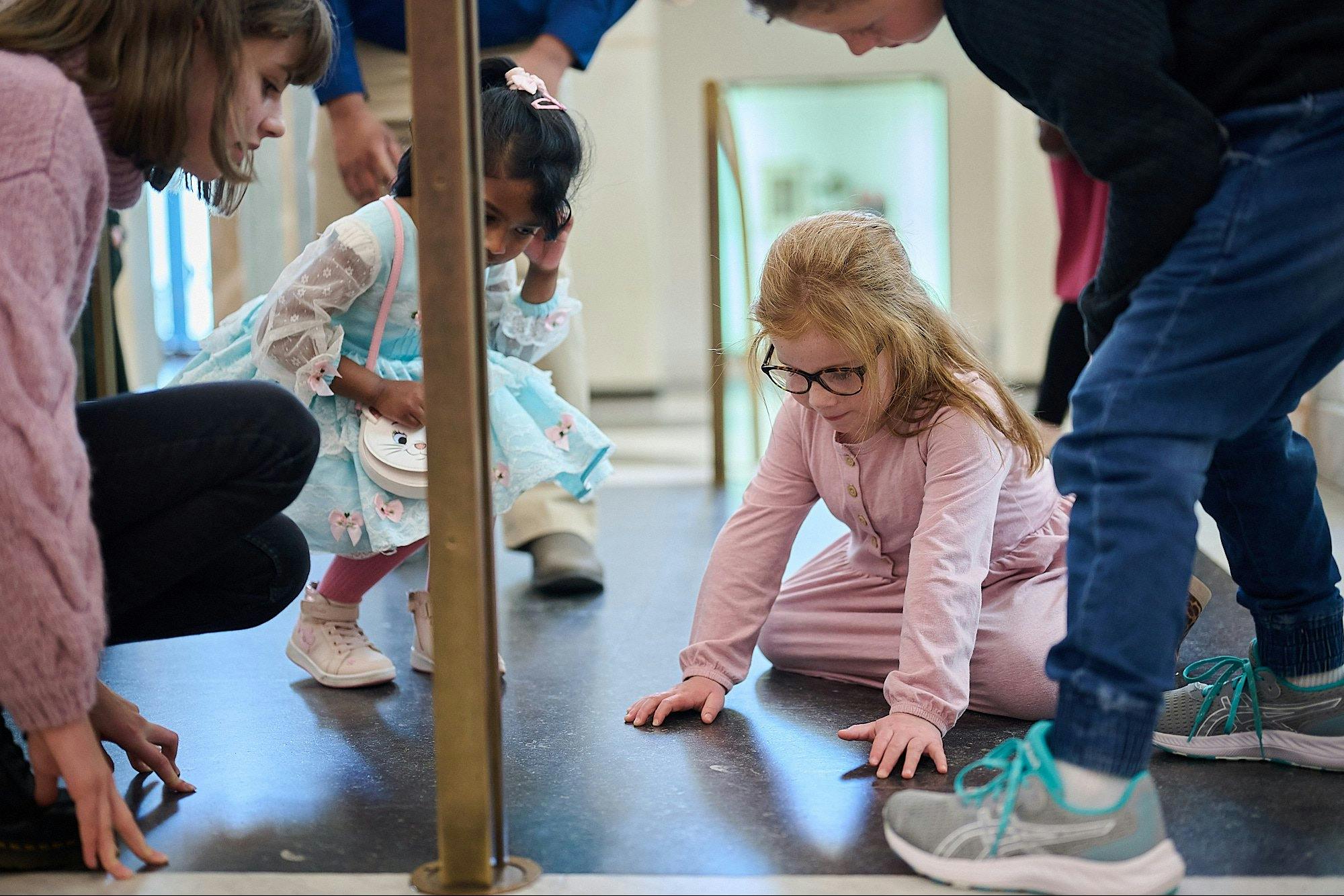 Children gather around to look at the Marble Foyer floor and a fossil within the marble floor
