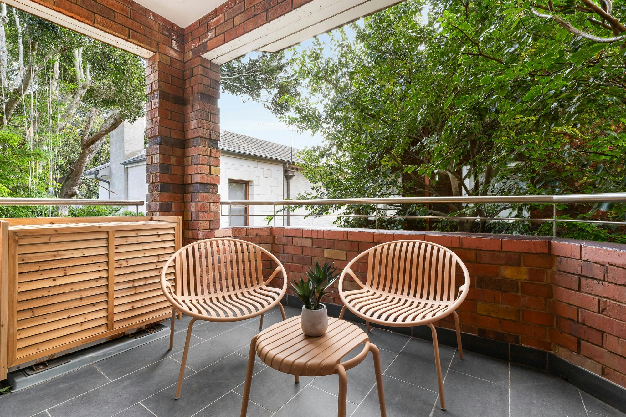 Spacious covered, paved balcony with rattan outdoor furniture set - 2 chairs and a small table.