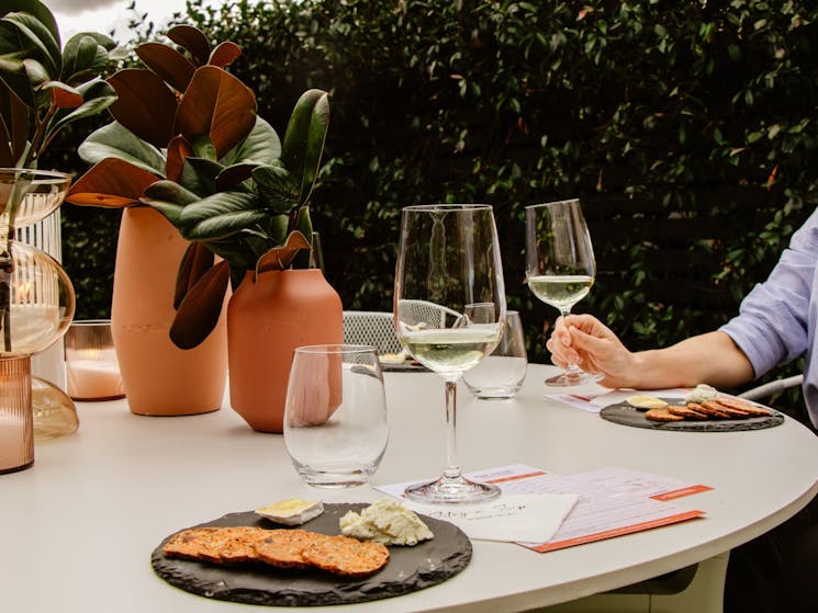 Hand reaching to pick up a wine tasting at a stylishly set table with lush green surrounds.