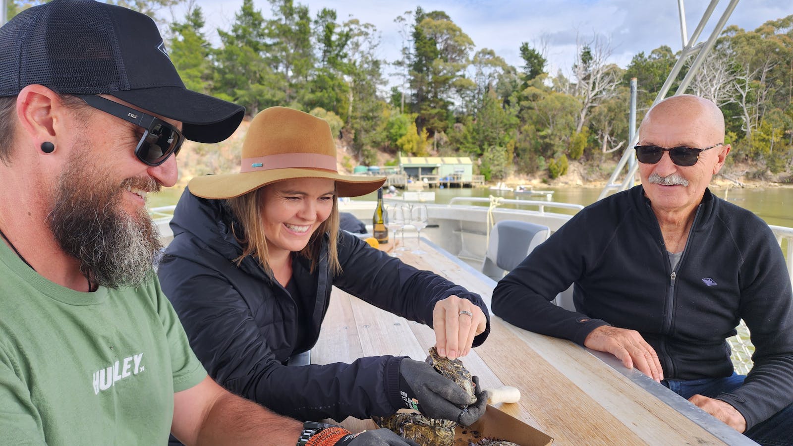 Guests aboard the TunaCorn laugh and shuck oysters by hand, on Tasmanian waters