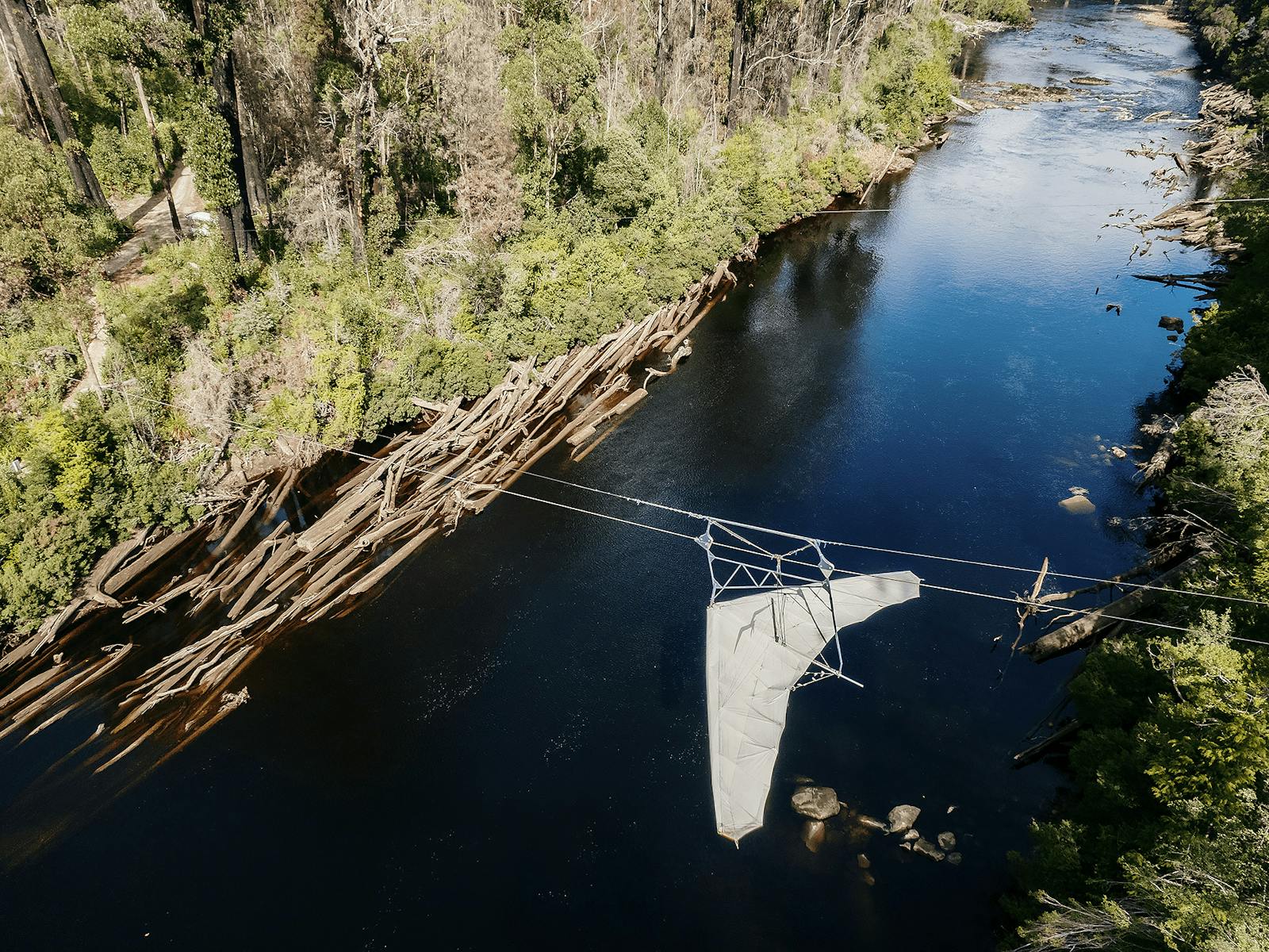Bird's eye view of zipline with harness, zooming over the river between tall trees.