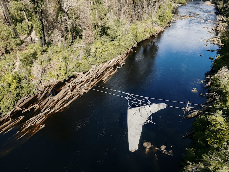 Bird's eye view of zipline with harness, zooming over the river between tall trees.