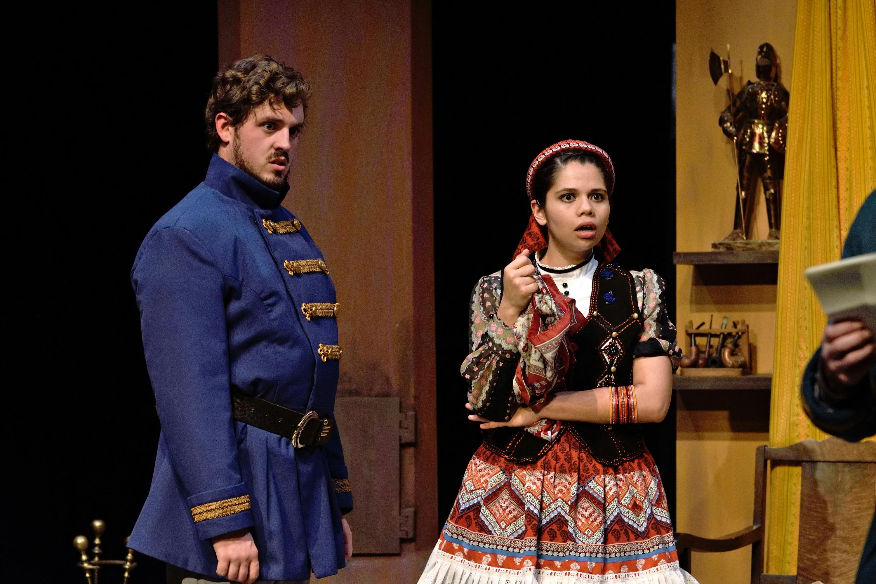 a young man in blue army coat and young girl in traditional Spanish dress look shocked
