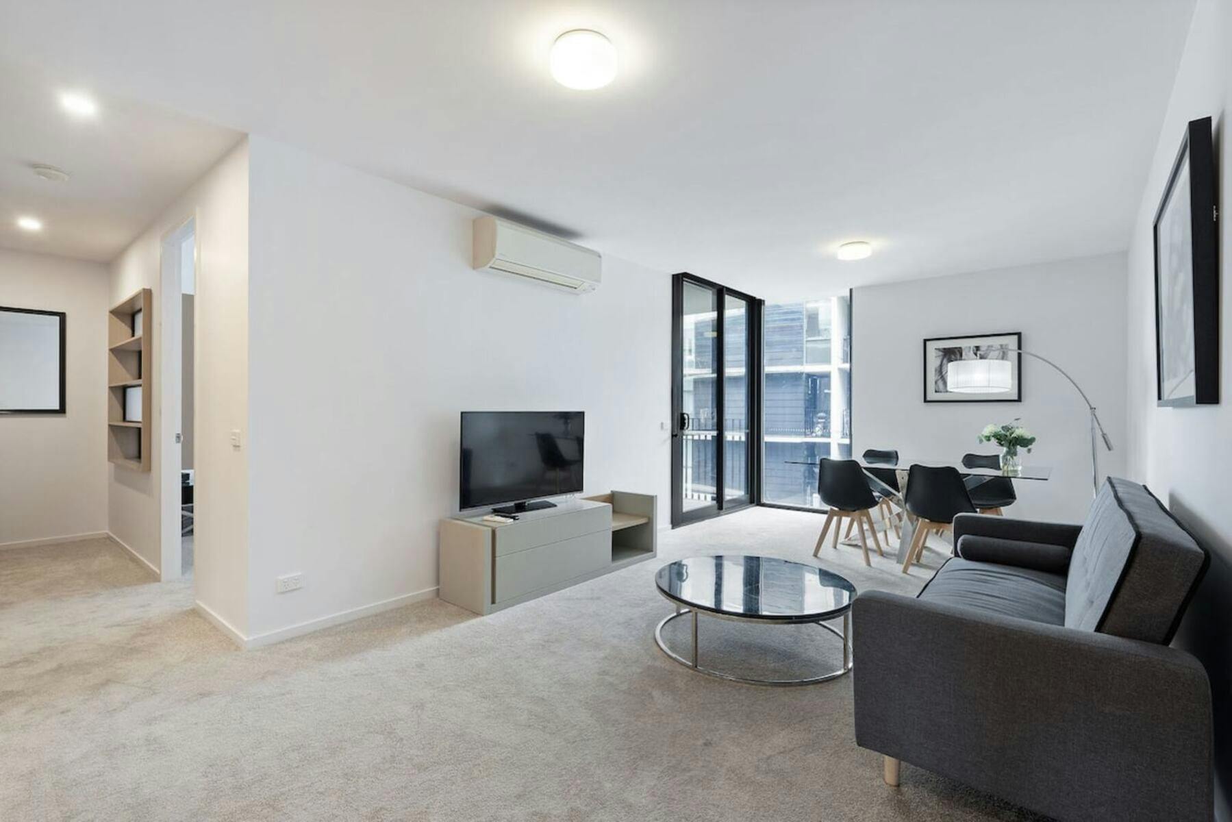 Modern apartment living room with grey sofa, TV, coffee table, and balcony doors.