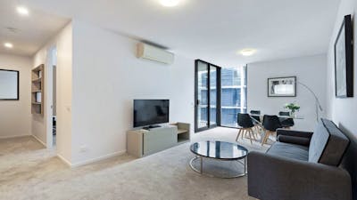 Modern apartment living room with grey sofa, TV, coffee table, and balcony doors.
