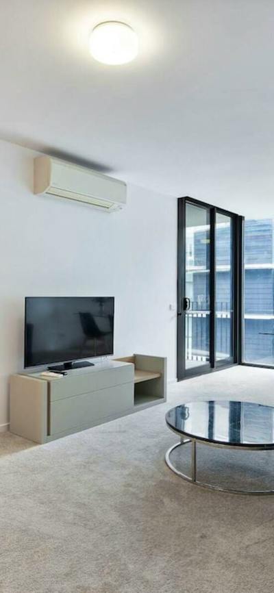 Modern apartment living room with grey sofa, TV, coffee table, and balcony doors.
