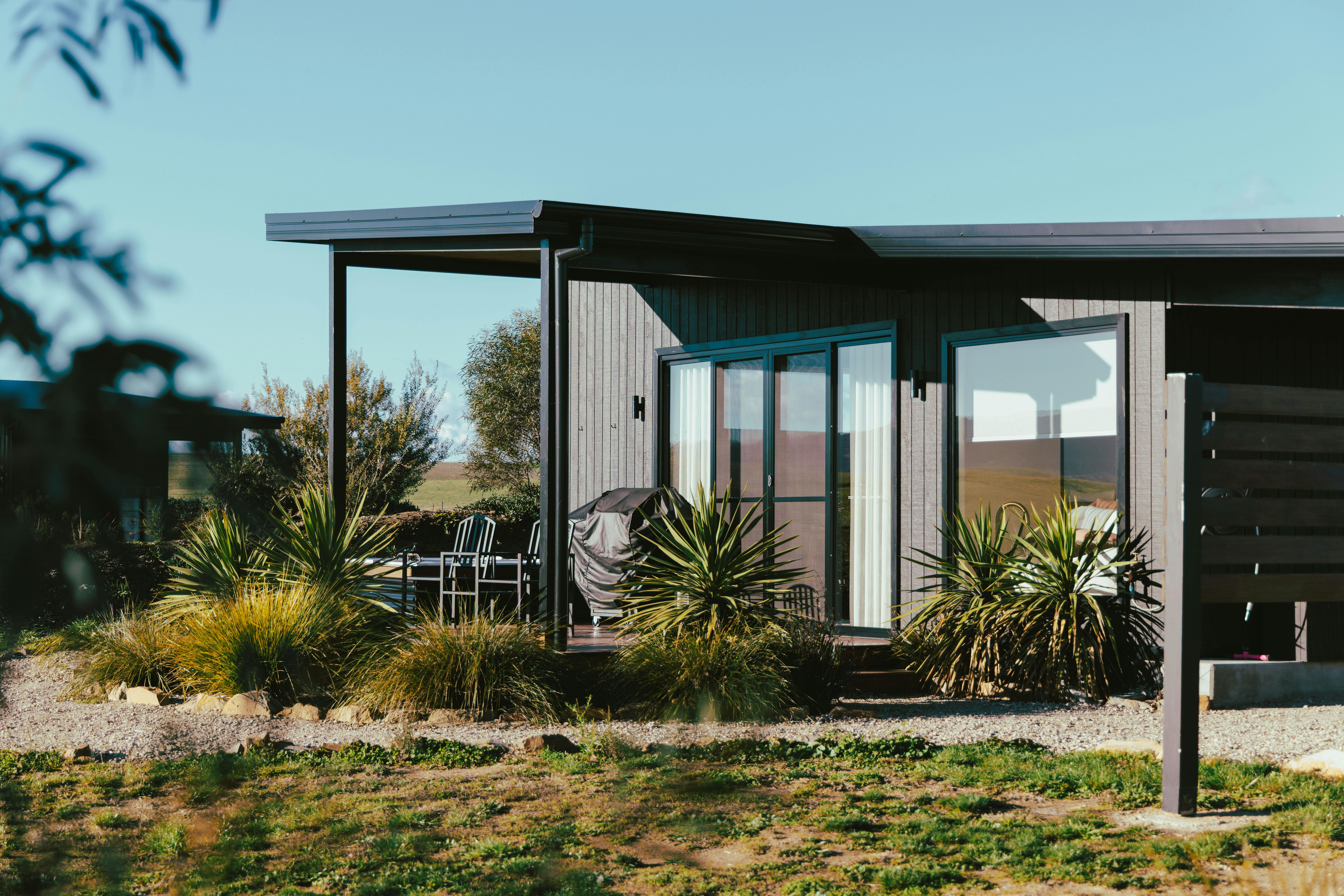A black, luxury studio with large glass windows and doors in a garden/rural setting.