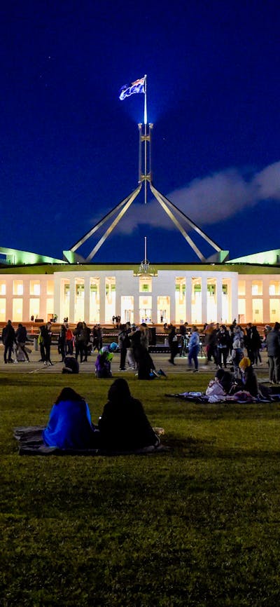 Night-time view of Australian Parliament House, brightly lit against a dark blue sky.
