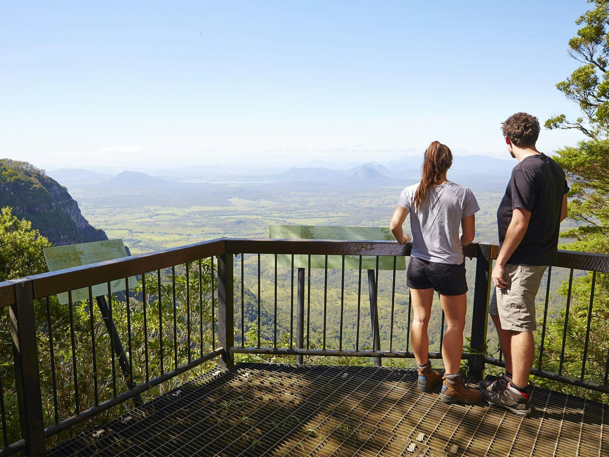 Two people standing at a lookout looking over and valley and mountains in the distance. Two people standing at a lookout looking over and valley and mountains in the distance.