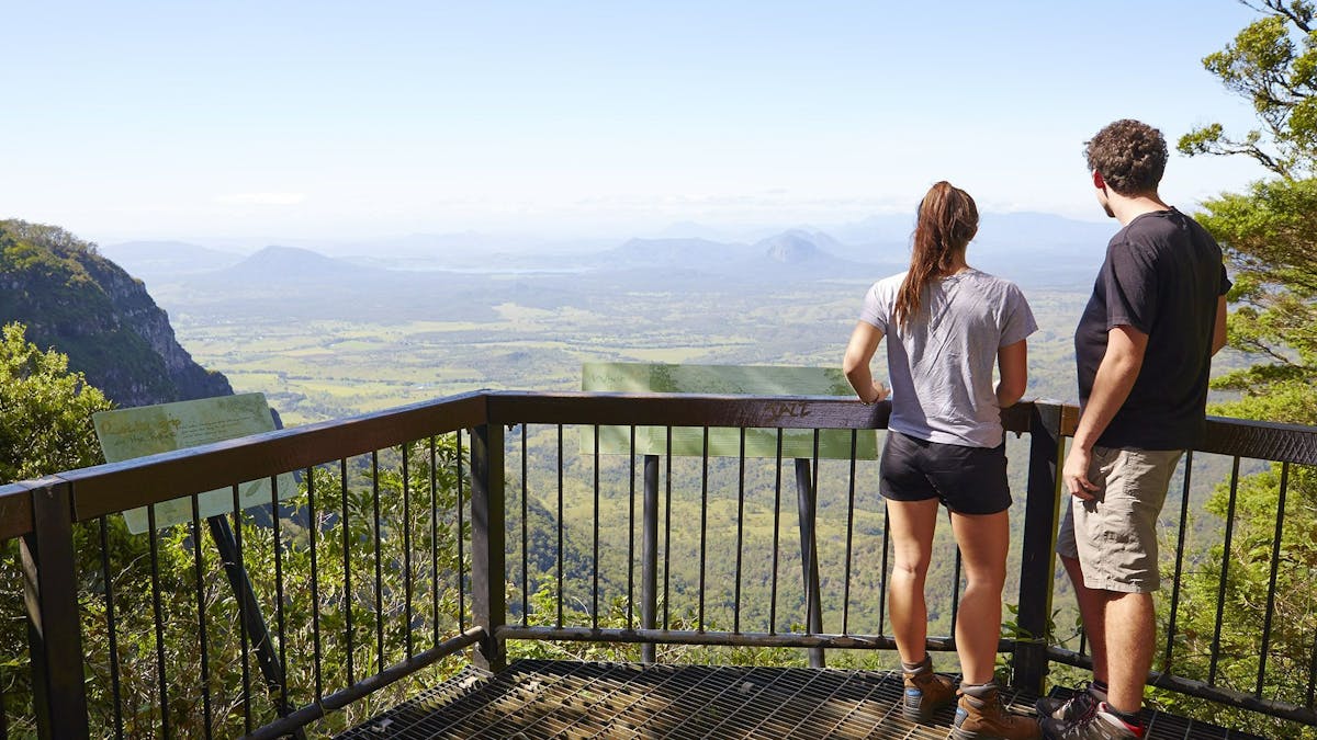 Two people standing at a lookout looking over and valley and mountains in the distance.