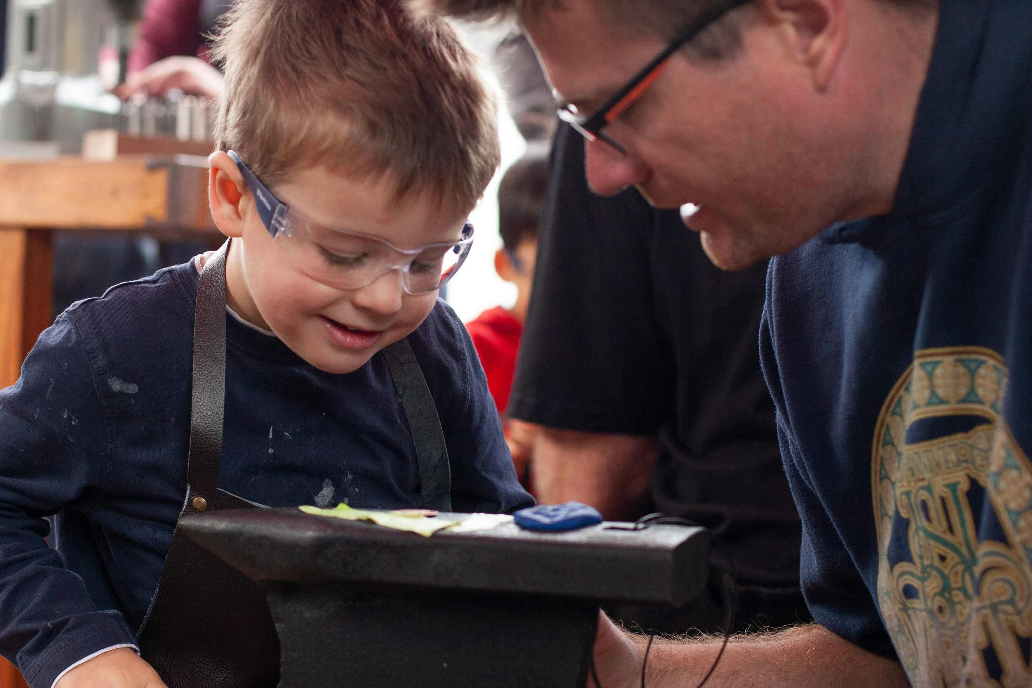 A child grips a hammer, striking playdough and anvil in the Kidsmith Zone.
